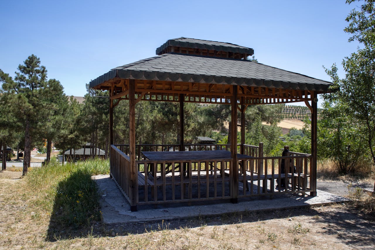 A wooden gazebo surrounded by lush pine trees in Pertek, Tunceli, Türkiye on a sunny day.